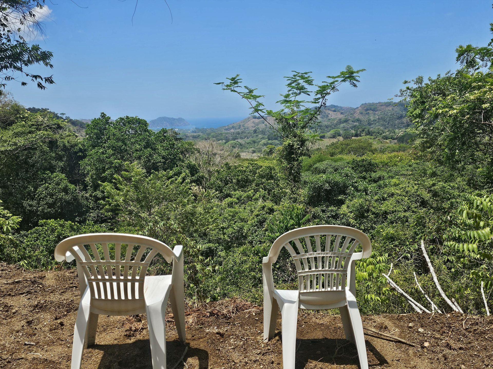 Two white plastic chairs at the edge of the cut, the valley and the ocean beyond